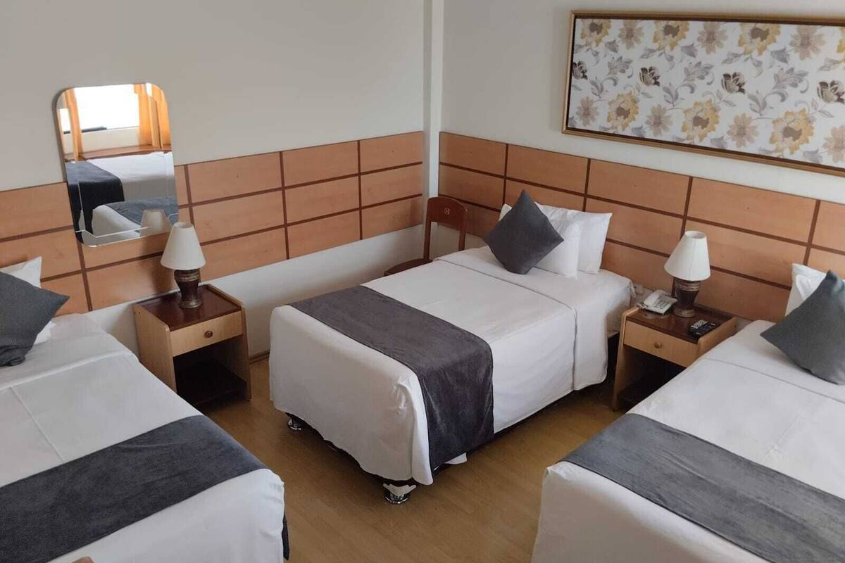 A hotel room with two single beds, a large mirror, a floral artwork on the wall, and a wooden headboard.