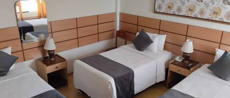 Habitación de hotel con dos camas individuales, un espejo grande, una obra de arte floral en la pared y un cabecero de madera.