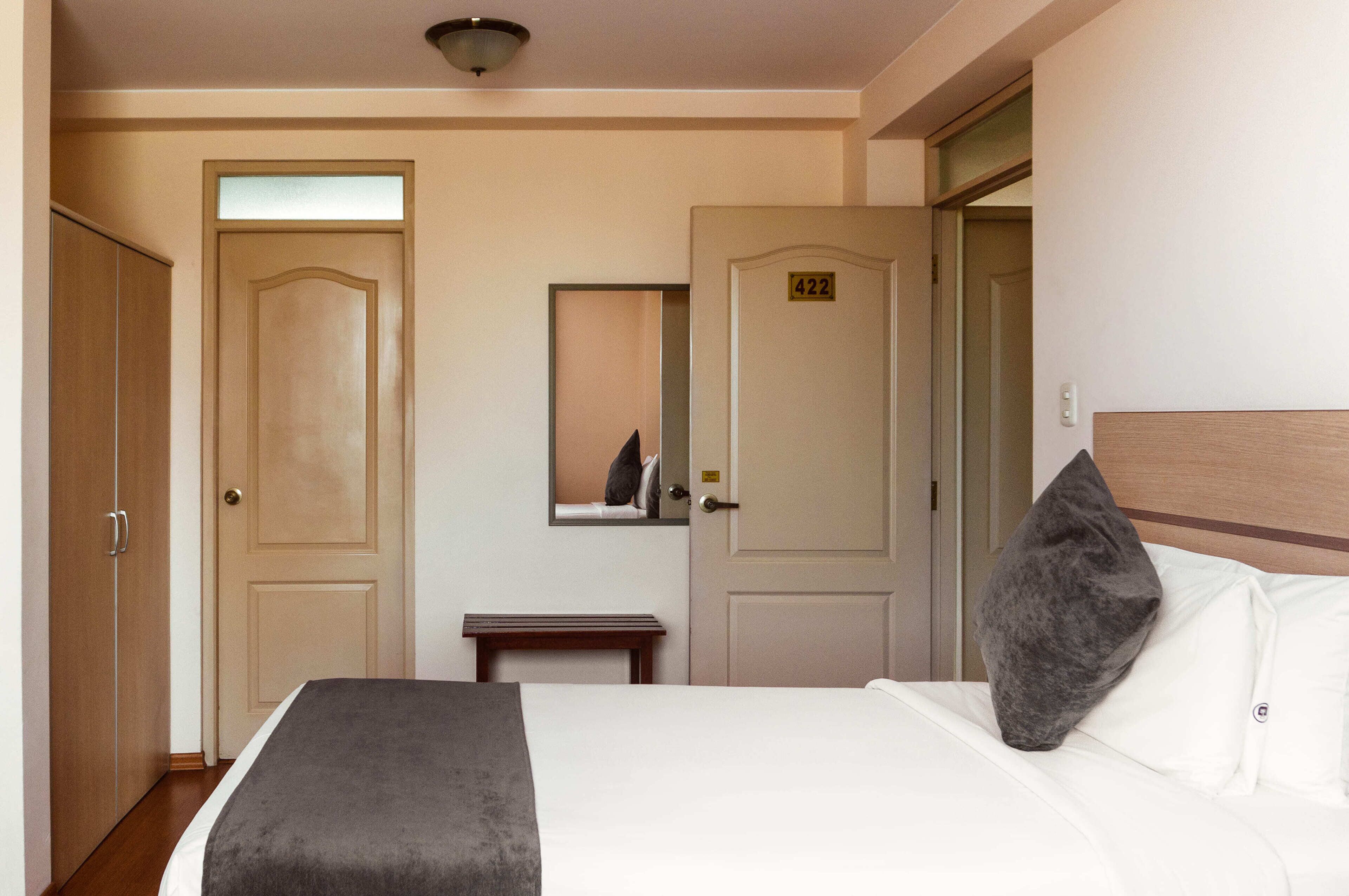 Une chambre d’hôtel avec un lit, une table de chevet, un miroir et deux portes.