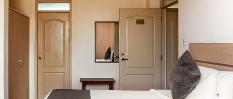 A hotel room with a bed, a bedside table, a mirror, and two doors.