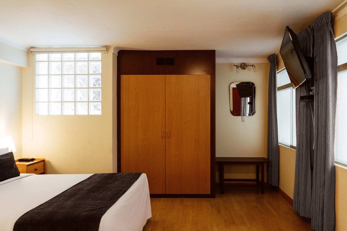 A hotel room with a bed, a wardrobe, a small table, a mirror, and a television.