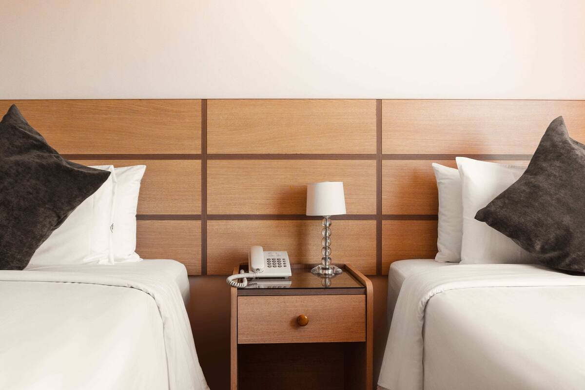 A hotel room with two beds, a nightstand with a phone and lamp, and a wooden headboard.