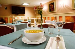 Una mesa de comedor con un tazón de sopa, una copa de vino y cubiertos.