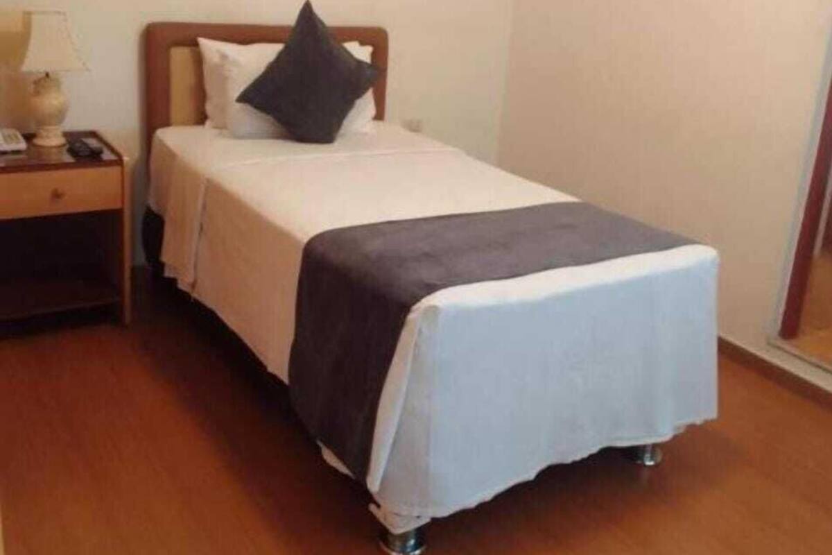 A single bed with a wooden headboard, a bedside table with a lamp, and a framed picture on the wall.