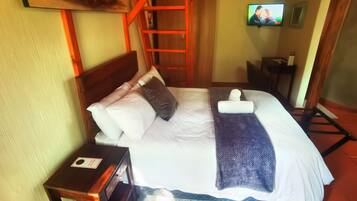 A neatly made bed with pillows and a blanket, a wooden nightstand with a card, a TV mounted on the wall, and a red ladder against the wall.
