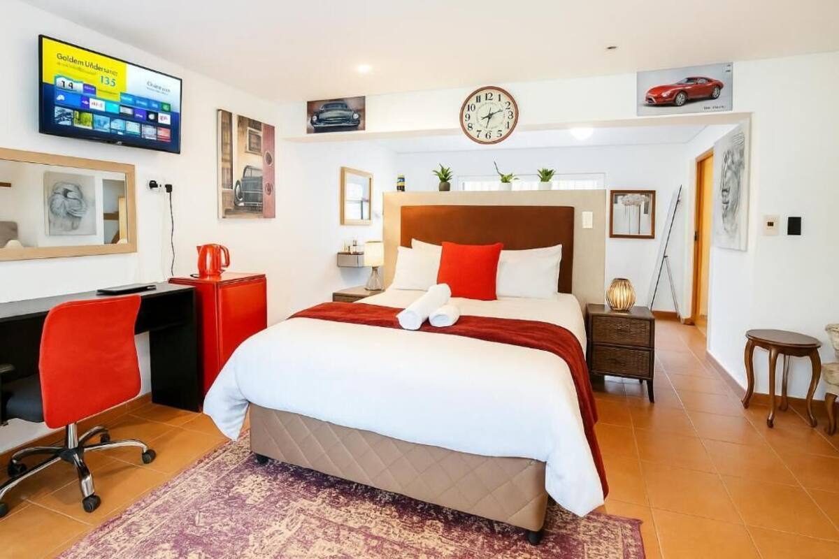 Habitación de hotel con una cama grande, un escritorio con una silla roja, un televisor en la pared y un reloj.