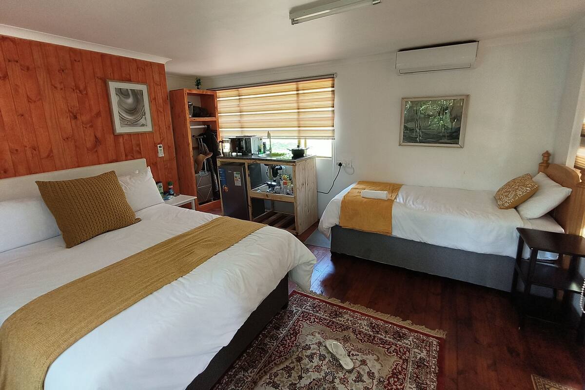 Una habitación de hotel con dos camas, un rincón americano, un revestimiento de madera y una ventana con persianas.