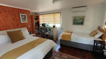 Une chambre d’hôtel avec deux lits, un coin cuisine, un mur en bois et une fenêtre avec des stores.