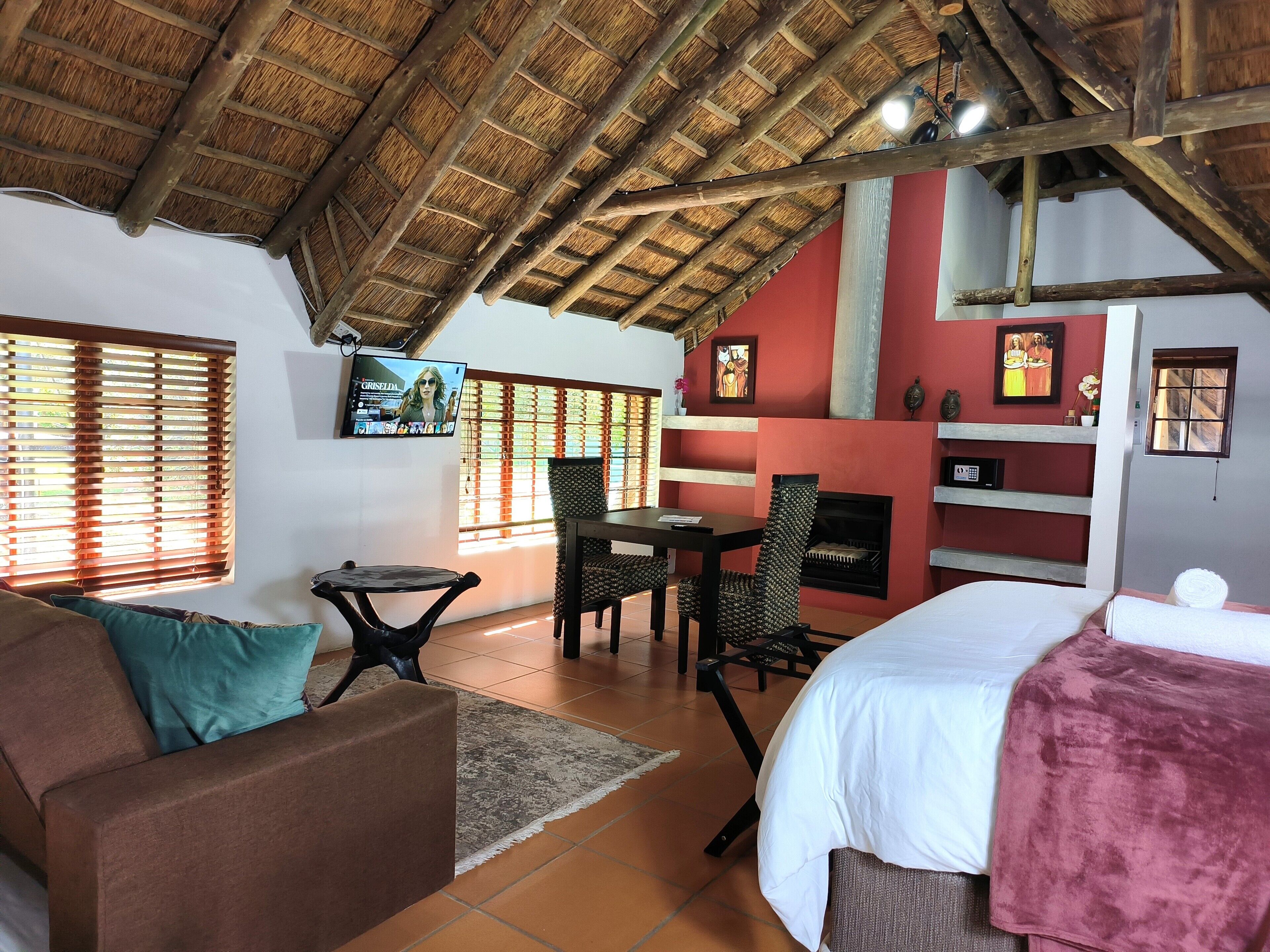 A cozy room with a thatched roof, a fireplace, a television, and a bed with a red blanket.