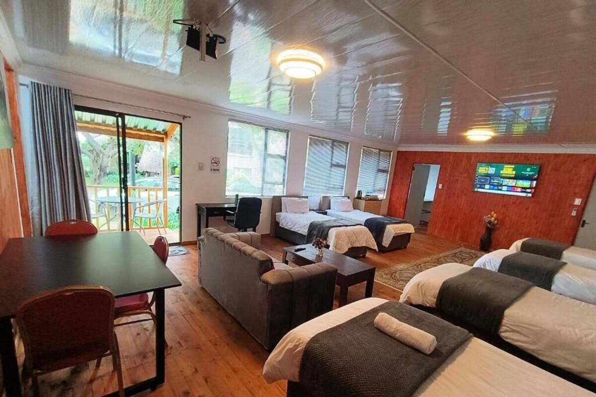 Habitación de hotel con piso de madera, una mesa de comedor con sillas, un sofá, dos camas, un televisor y vista al exterior.