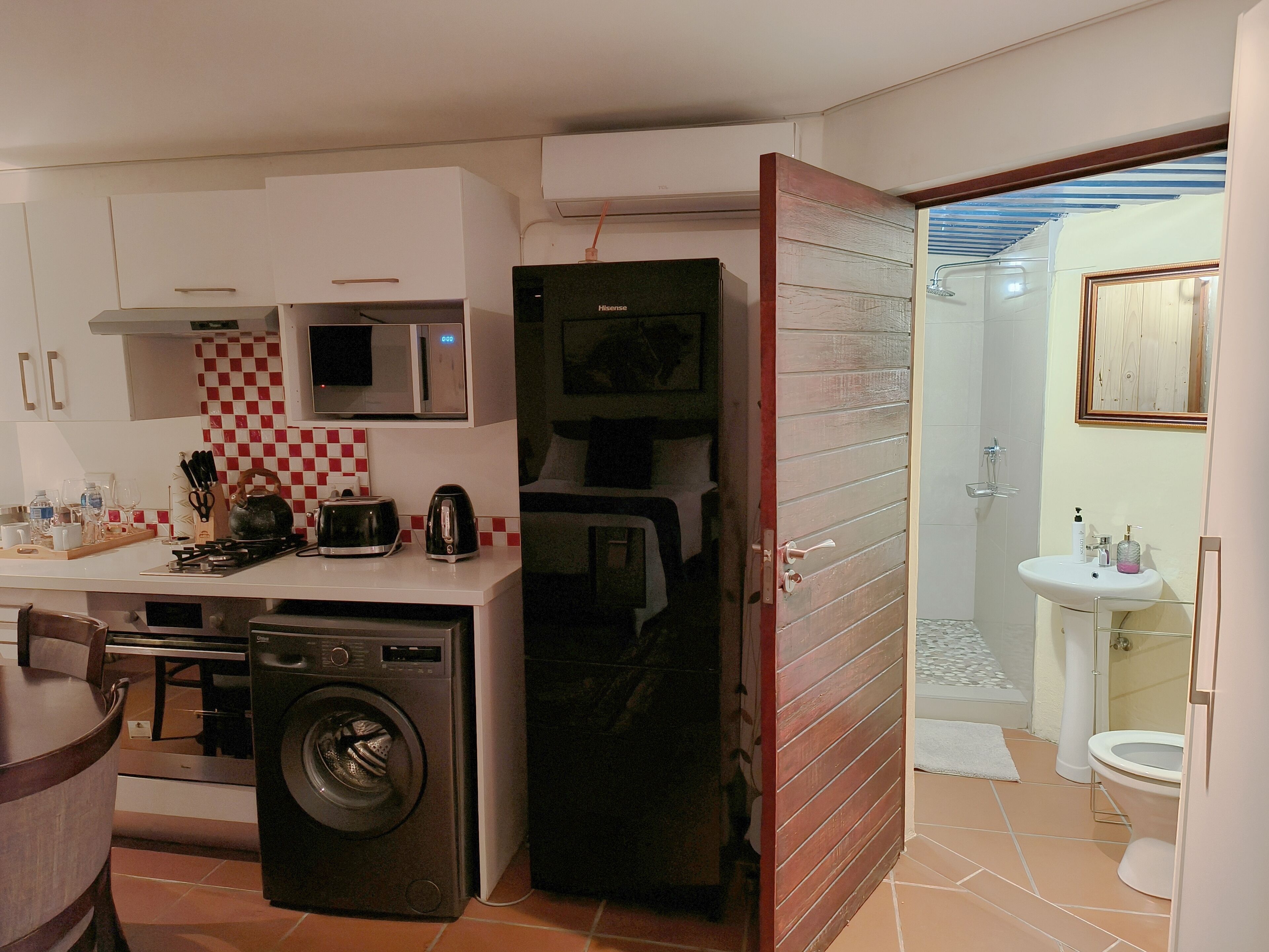 A compact kitchen with a microwave, toaster, kettle, and washing machine. It includes a small dining area with a table and chairs.