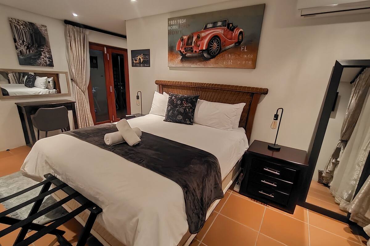Una habitación de hotel con cama, escritorio, silla, mesita de noche y un cuadro en la pared.