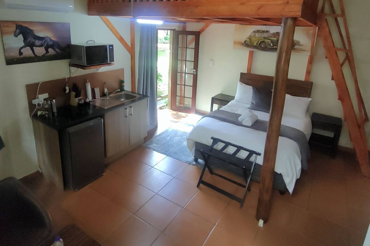 Un dormitorio con cama elevada, una kitchenette pequeña y un comedor.