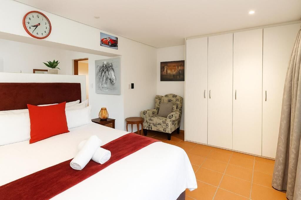 A hotel room with a bed, a clock, a chair, and a wardrobe.