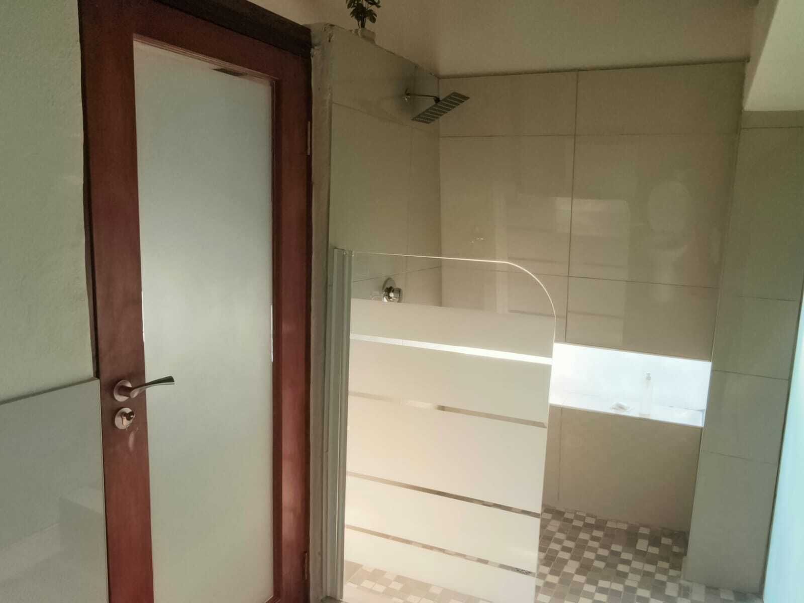 A bathroom with a glass shower enclosure, a tiled floor, and a wooden door.
