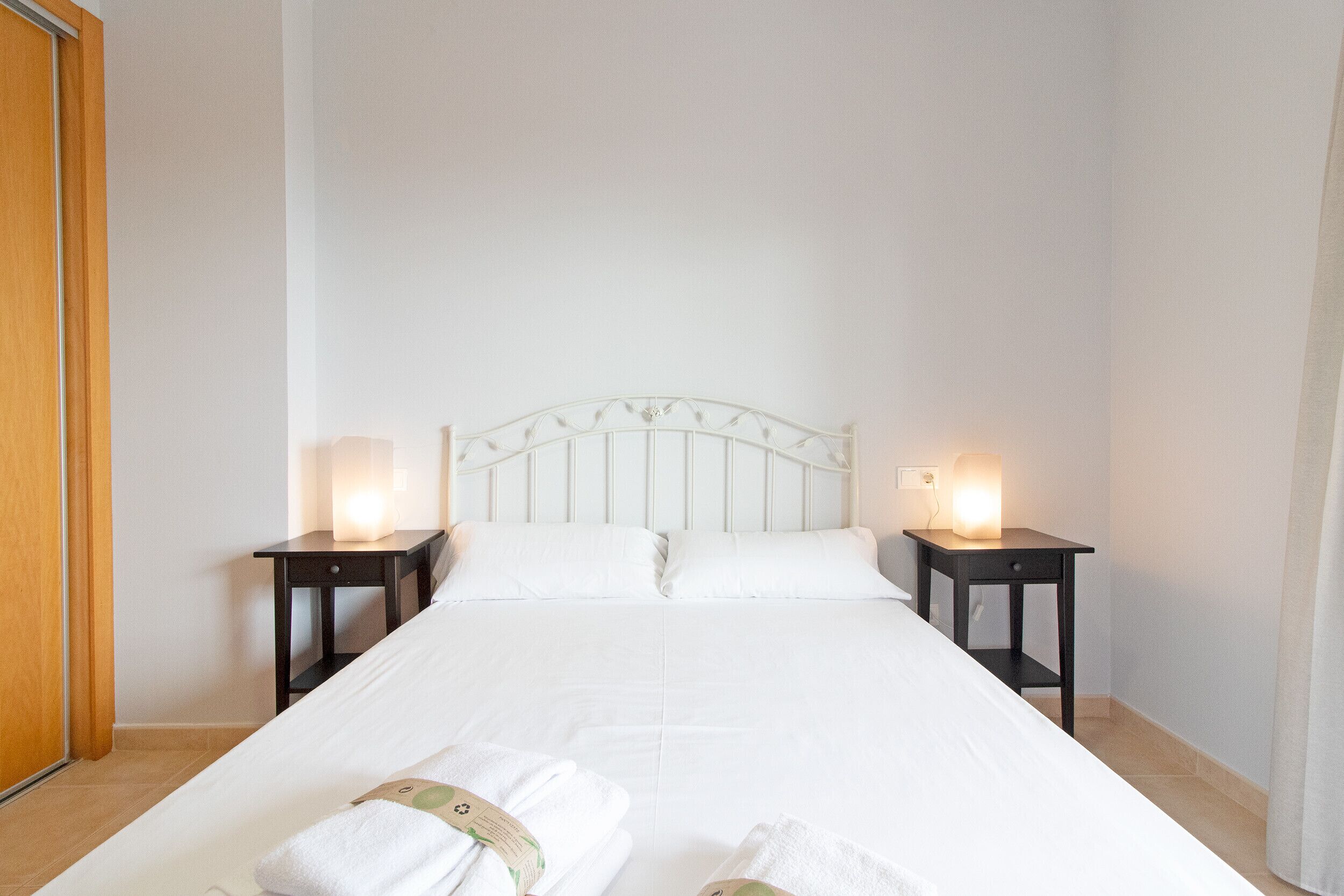 A neatly made bed with white linens and two bedside tables with lamps.