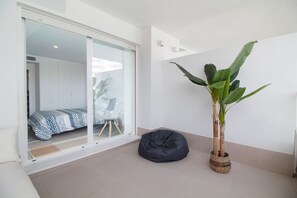 A modern room with a sliding glass door leading to a bedroom, a black bean bag chair, and a large potted plant. - Global Vacacional: Apartment with terrace and pool views in Gran Canet (Canet d´en berenguer)