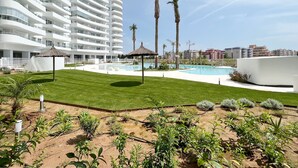 A modern hotel with a large pool, palm trees, and a well-maintained lawn. - Global Vacacional: Apartment with terrace and pool views in Gran Canet (Canet d´en berenguer)