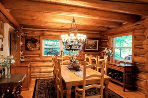 Interior rústico de cabana de madeira com mesa de jantar, cadeiras, um candelabro e uma estante para vinho.