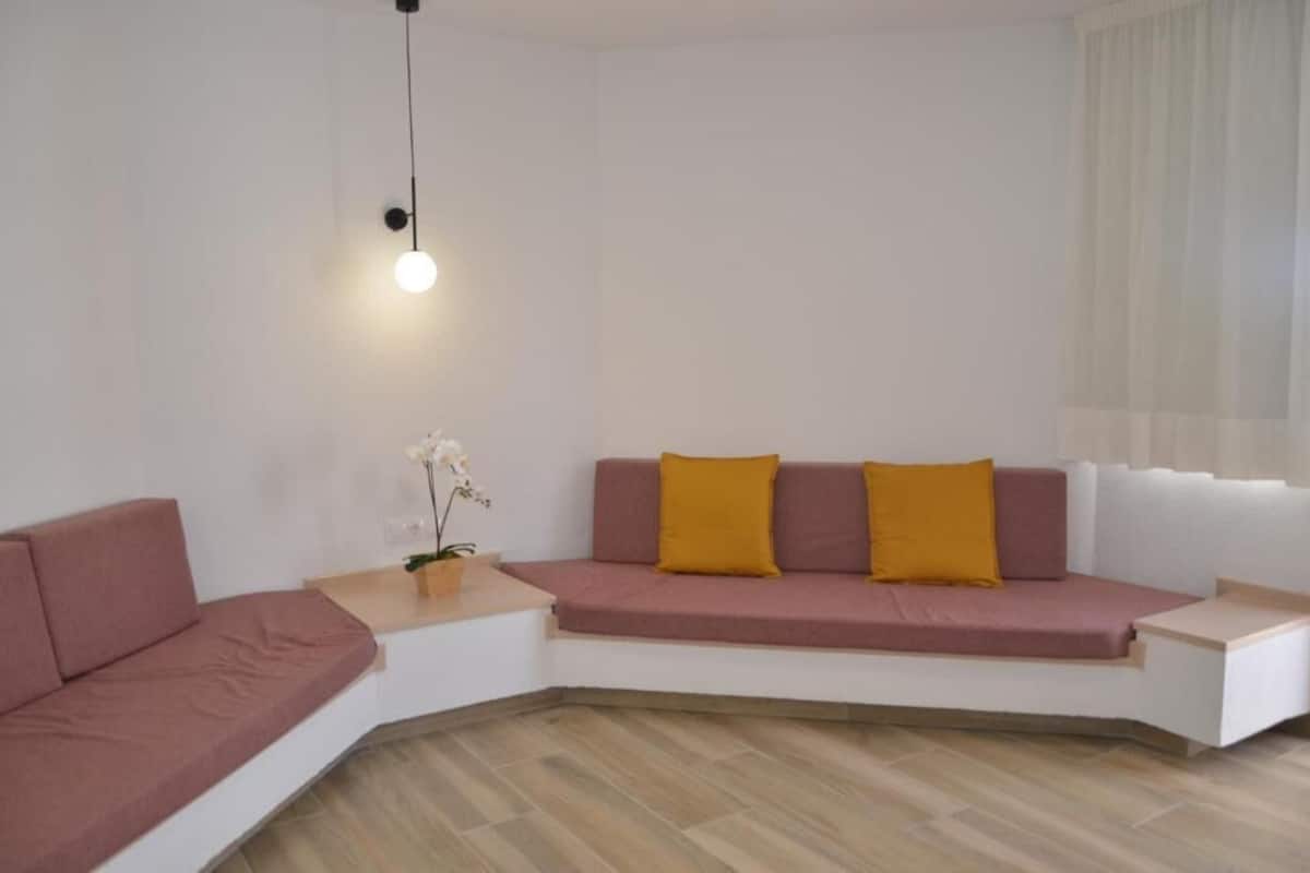 Ein modernes Wohnzimmer mit einem rosa Sofa, einem weißen Couchtisch und einer Pendelleuchte.