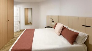 Een hotelkamer met een bed, een houten garderobe, een spiegel en een nachtkastje.