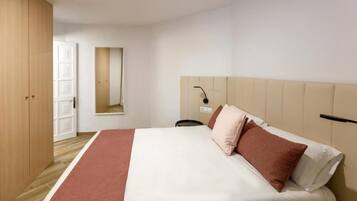 A hotel room with a bed, a wooden wardrobe, a mirror, and a bedside table.
