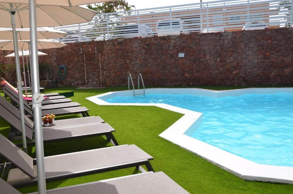 A swimming pool with lounge chairs and umbrellas, surrounded by a stone wall and green lawn.