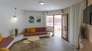 Un salon moderne avec un canapé, deux petites tables, un téléviseur et un balcon offrant une vue agréable.