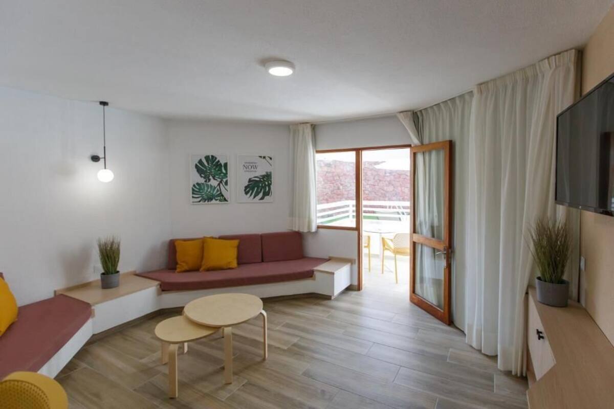 Ein modernes Wohnzimmer mit einer Couch, zwei kleinen Tischen, einem Fernseher und einem Balkon mit Blick.