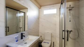 A bathroom with a white sink, a mirror, a toilet, a shower with a glass door, and a window.