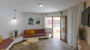 A modern living room with a sofa, two small tables, a TV, and a balcony with a view.