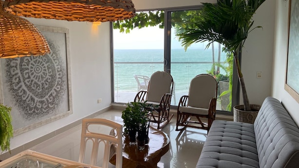 A modern living room with a view of the ocean, a grey sofa, wicker lamps, and a dining area with white chairs. - Cartagena Frente a la Playa 27A (Cartagena)
