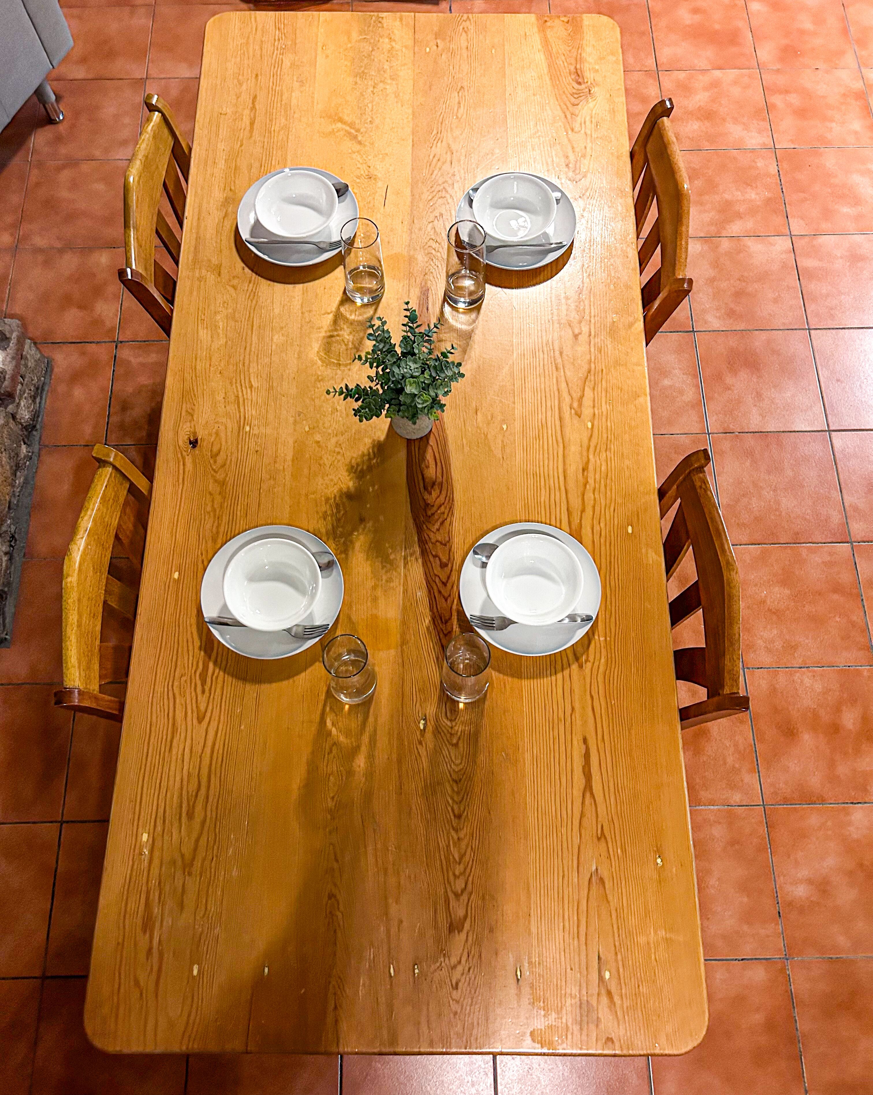 Un tavolo da pranzo in legno con quattro sedie, una pianta in vaso e due bicchieri d'acqua.
