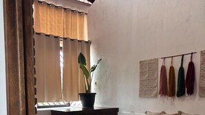 Une chambre à coucher avec un lit, une plante en pot, un bureau et une fenêtre avec des rideaux.