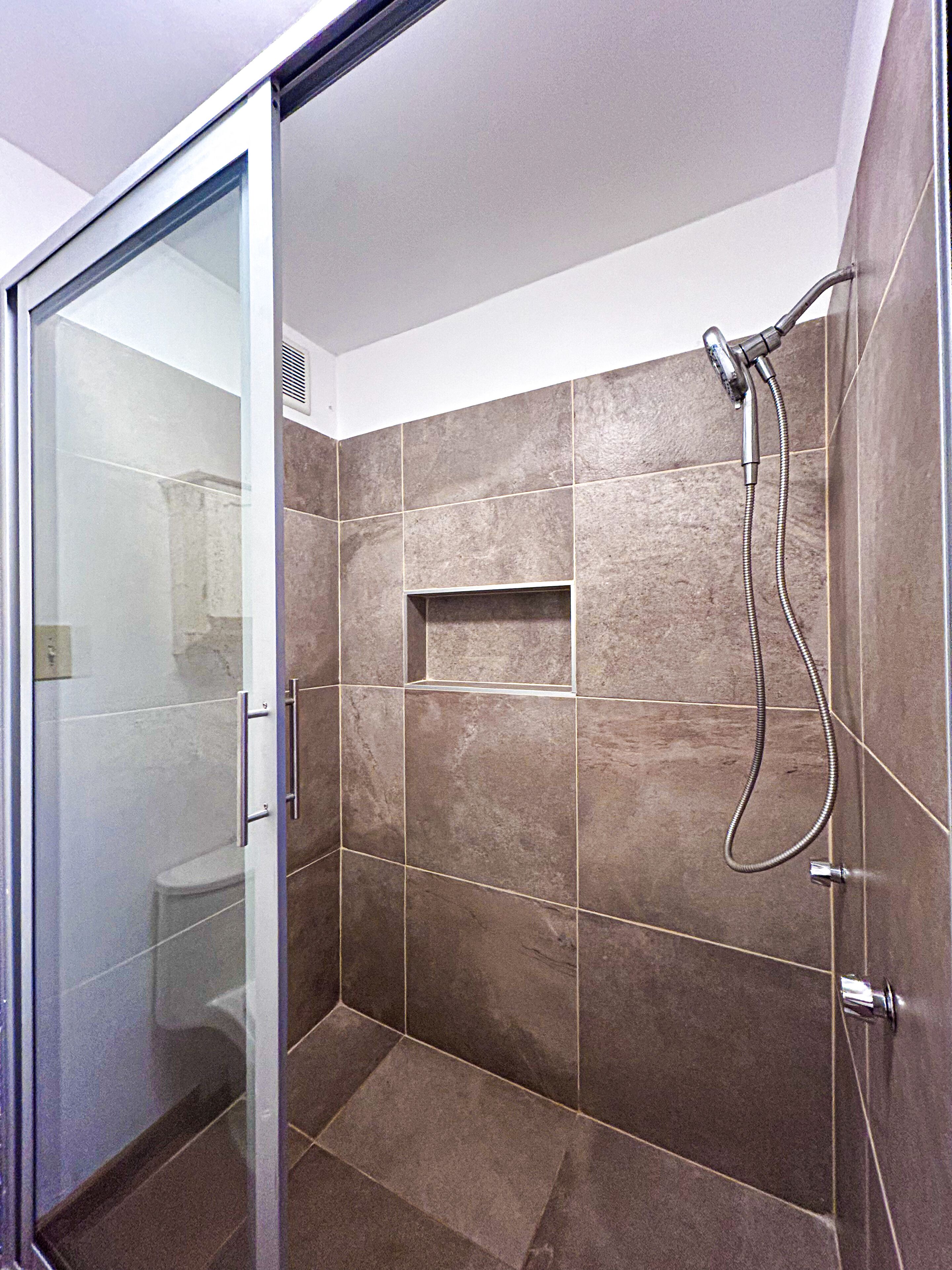Une salle de bain moderne avec une porte de douche en verre, des murs carrelés et une étagère intégrée.