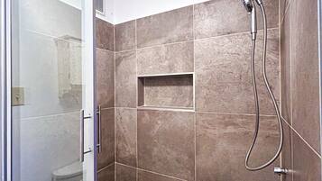 Une salle de bain moderne avec une porte de douche en verre, des murs carrelés et une étagère intégrée.