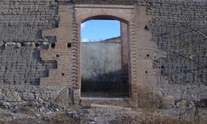 Ein Backsteinbogen führt in ein Gebäude mit rustikalem, unfertigem Innenraum.