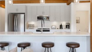 Una cocina moderna con armarios blancos, electrodomésticos de acero inoxidable y una isla central con taburetes.