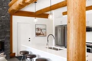 A modern kitchen with a stainless steel refrigerator, a white countertop, and a wooden ceiling beam.