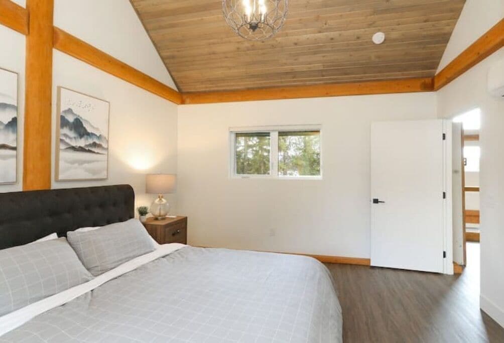 Un dormitorio con cama, techo de madera, una ventana y una puerta.