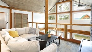 Un salón comedor amplio con un sofá grande, una mesa de centro y vistas a una casa a través de ventanas grandes.