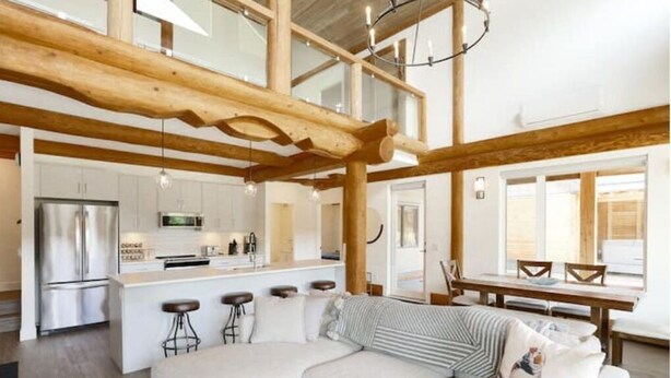 Una cocina moderna con electrodomésticos de acero inoxidable, una isla central con taburetes y un comedor con mesa y sillas de madera.