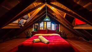 An attic bedroom with a red bed, wooden beams, and a skylight. - Le Chateau Hostal & Spa (Guatapé)