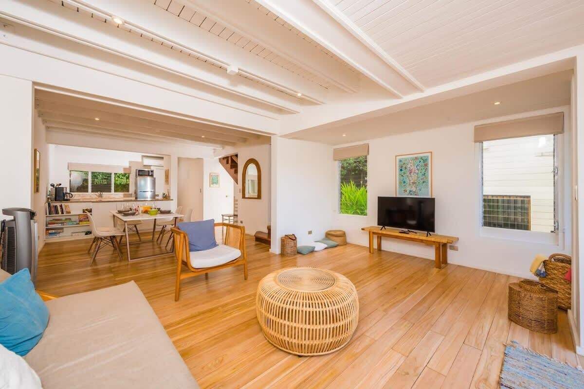 A spacious living area with a wooden floor, a round wicker ottoman, a sofa, and a television.