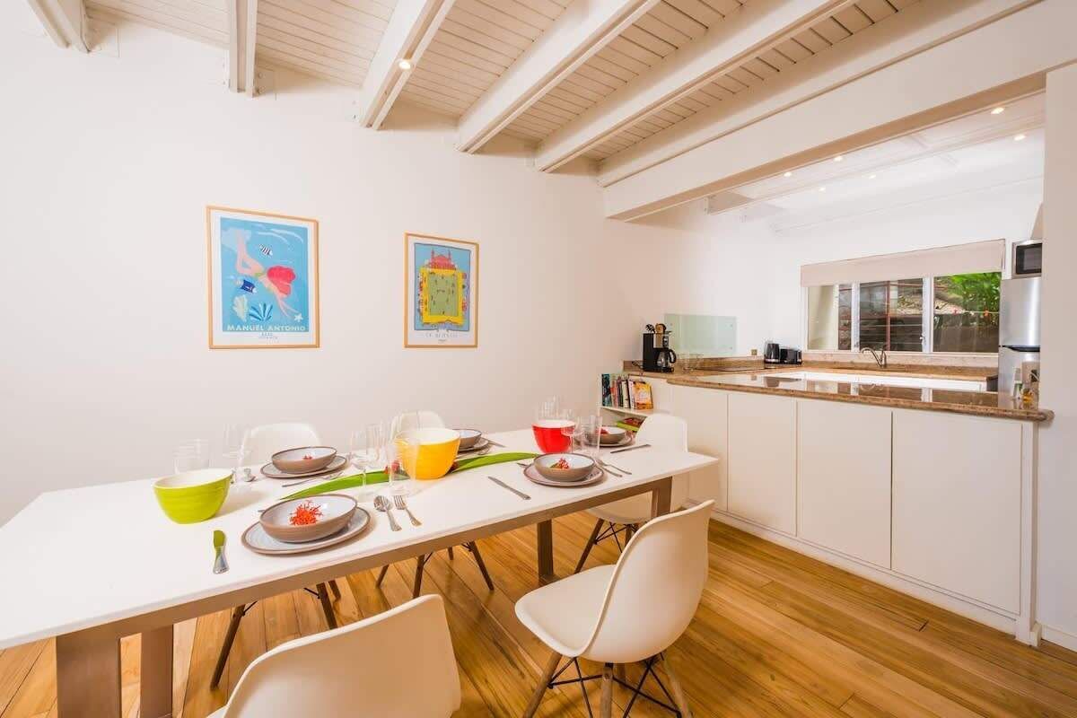A modern kitchen with white cabinets, a dining table set for four, and two framed artworks on the wall.