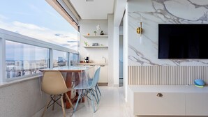 A modern kitchen with a large window, a dining area with chairs, and a TV mounted on a marble wall. - Modern Apartment with Fantastic View of the Flamboyant  (Goiânia)