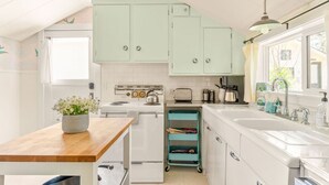 A kitchen with white cabinets, a wooden countertop, a stove, a sink, and a window. - The Sparrow Cottage (Bend)