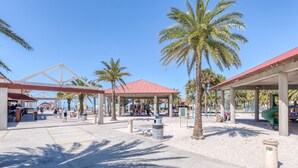 Un espacio público al aire libre con un pabellón techado, palmeras y un parque infantil.
