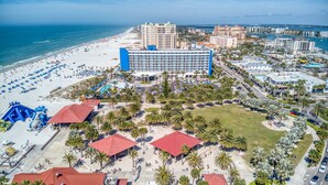 Vista aérea de un complejo turístico costero con un hotel grande, playa y palmeras.