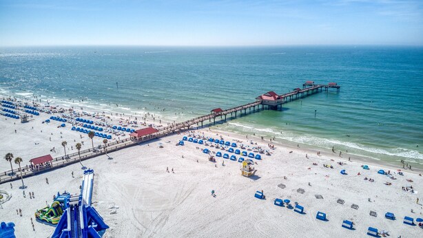 A beach with a long pier extending into the ocean, numerous umbrellas, and a lifeguard tower. - 403, Water View-Clearwater Bch in 6 min, Pool/Gym (Clearwater Beach)